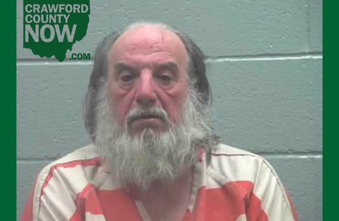 Mugshot of an older man with a long gray beard in an orange-and-white striped jumpsuit, against a gray cinder-block wall; Crawford County Now logo in the upper left.