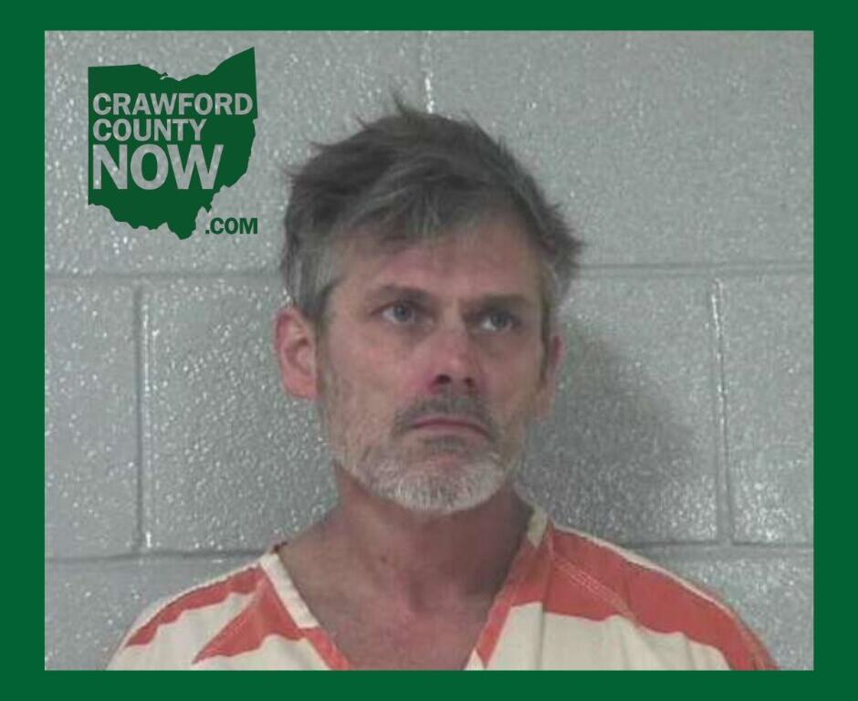 Mugshot of a middle-aged man with gray hair and stubble in an orange-and-white striped jail jumpsuit, standing against a gray cinder block wall; Crawford County Now logo in the upper left corner.