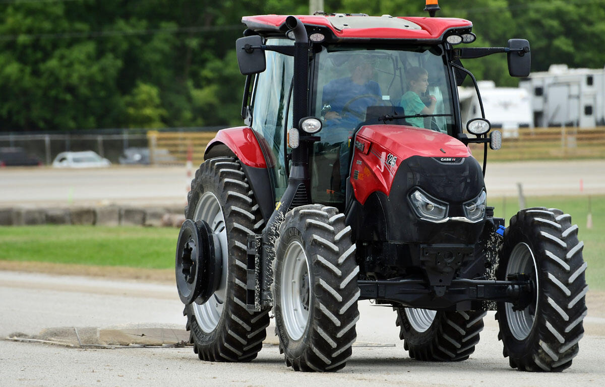Red agricultural tractor with oversized front and rear tires parked on a paved lot, two people visible inside the cab.