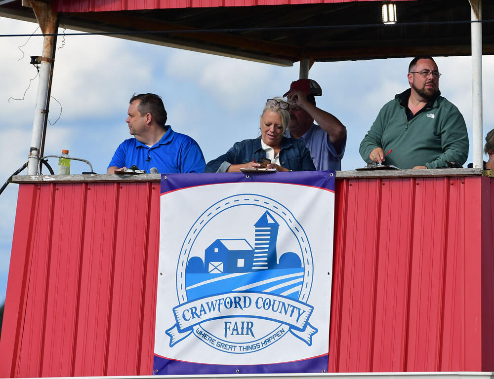Group of people in a red elevated booth at a Crawford County Fair, banner visible