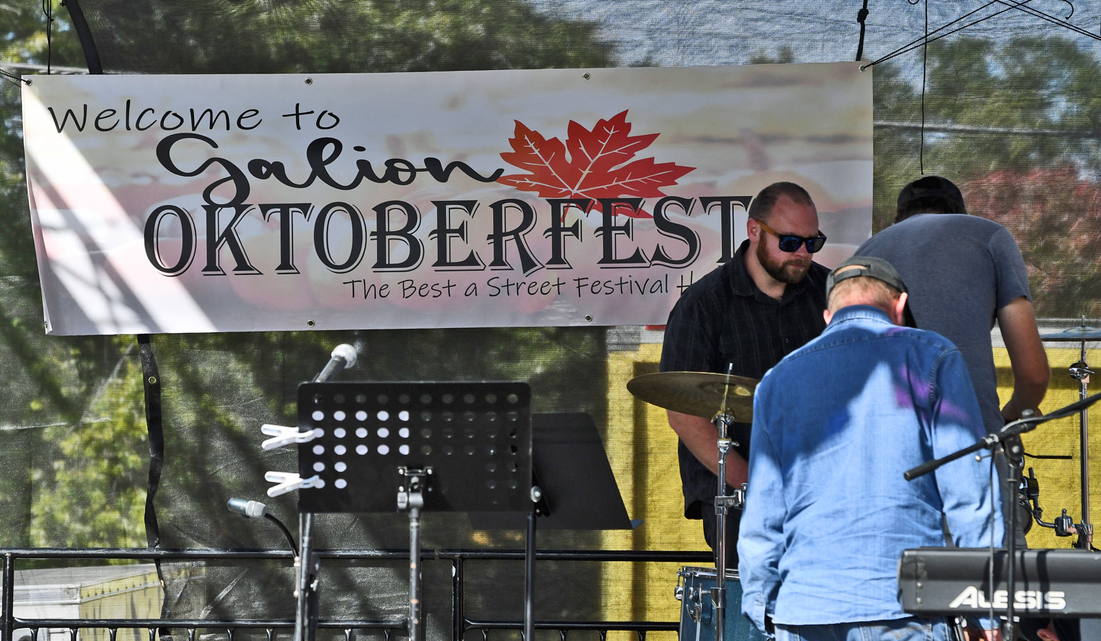 Stage at Galion Oktoberfest with a banner reading 'Welcome to Galion Oktoberfest' and a small band setup including a drummer and keyboard on the right side.