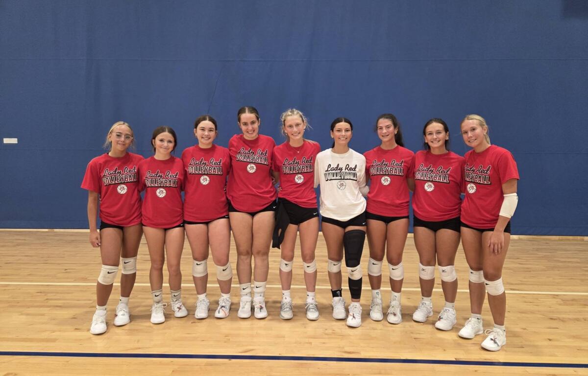 Group of young female volleyball players in red shirts reading 'Lady Red Volleyball' posing together in a gym.
