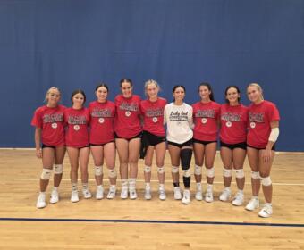 Group of young female volleyball players in red shirts reading 'Lady Red Volleyball' posing together in a gym.